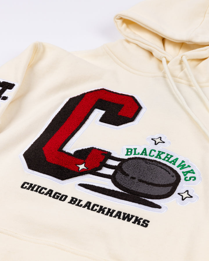 cream Mitchell & Ness hoodie with Chicago Blackhawks C and puck graphic embroidered on front with est. 1926 embroidered on right sleeve and secondary logo on left sleeve - front detail lay flat