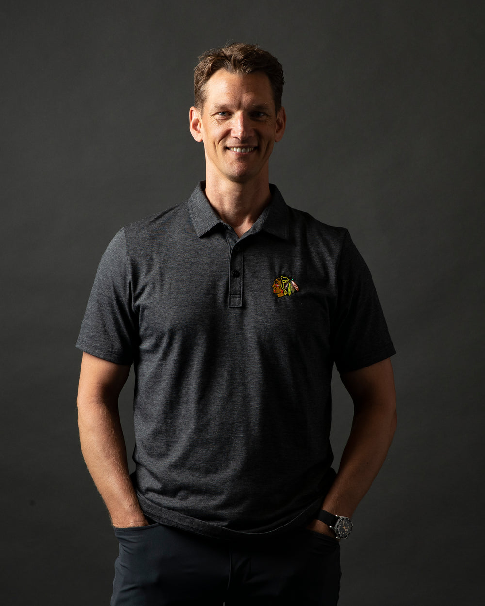 dark grey TravisMathew polo with button closure and embroidered Chicago Blackhawks primary logo on left chest - on Mark Eaton, Assistant GM Player Development for the Chicago Blackhawks