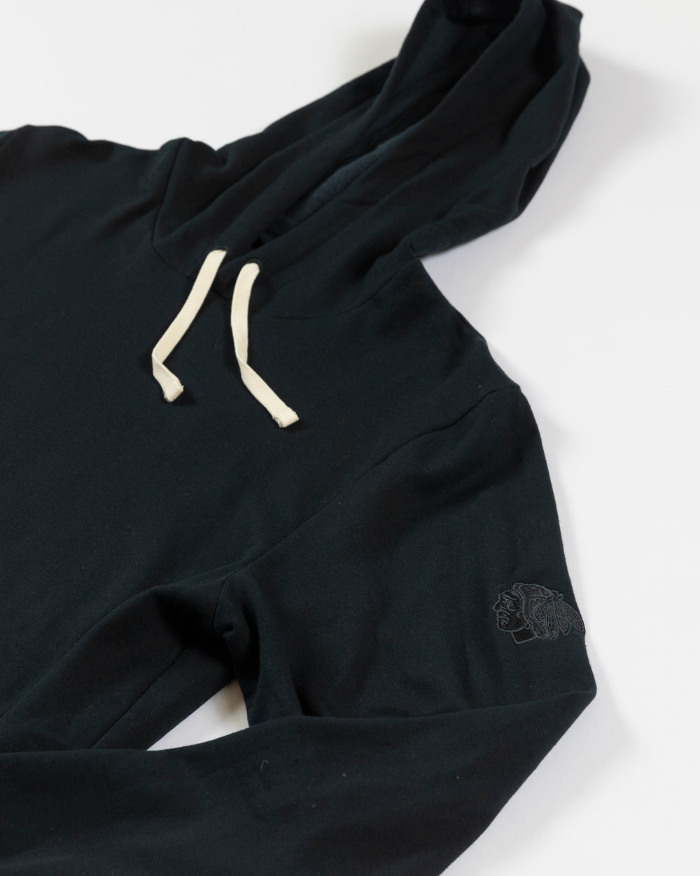 TravisMathew black Chicago Blackhawks hoodie with white drawstring and embroidered tonal primary logo on left shoulder - detail