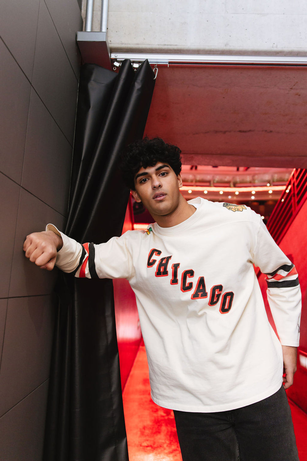 man wearing cream Alice & Wonder long sleeve tee with diagonal Chicago wordmark graphic and Chicago Blackhawks secondary and primary logo on shoulders with jersey stripes on sleeves