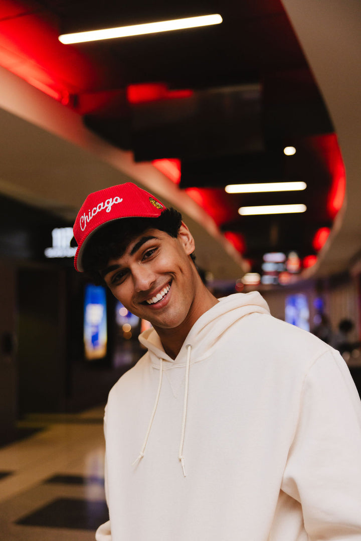 man wearing red corduroy Alice & Wonder adjustable hat with white chainstitched Chicago script graphic on front and Chicago Blackhawks primary logo on left side