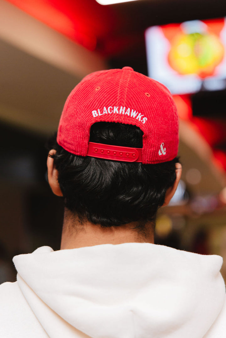 man wearing red corduroy Alice & Wonder adjustable hat with white chainstitched Chicago script graphic on front and Chicago Blackhawks primary logo on left side