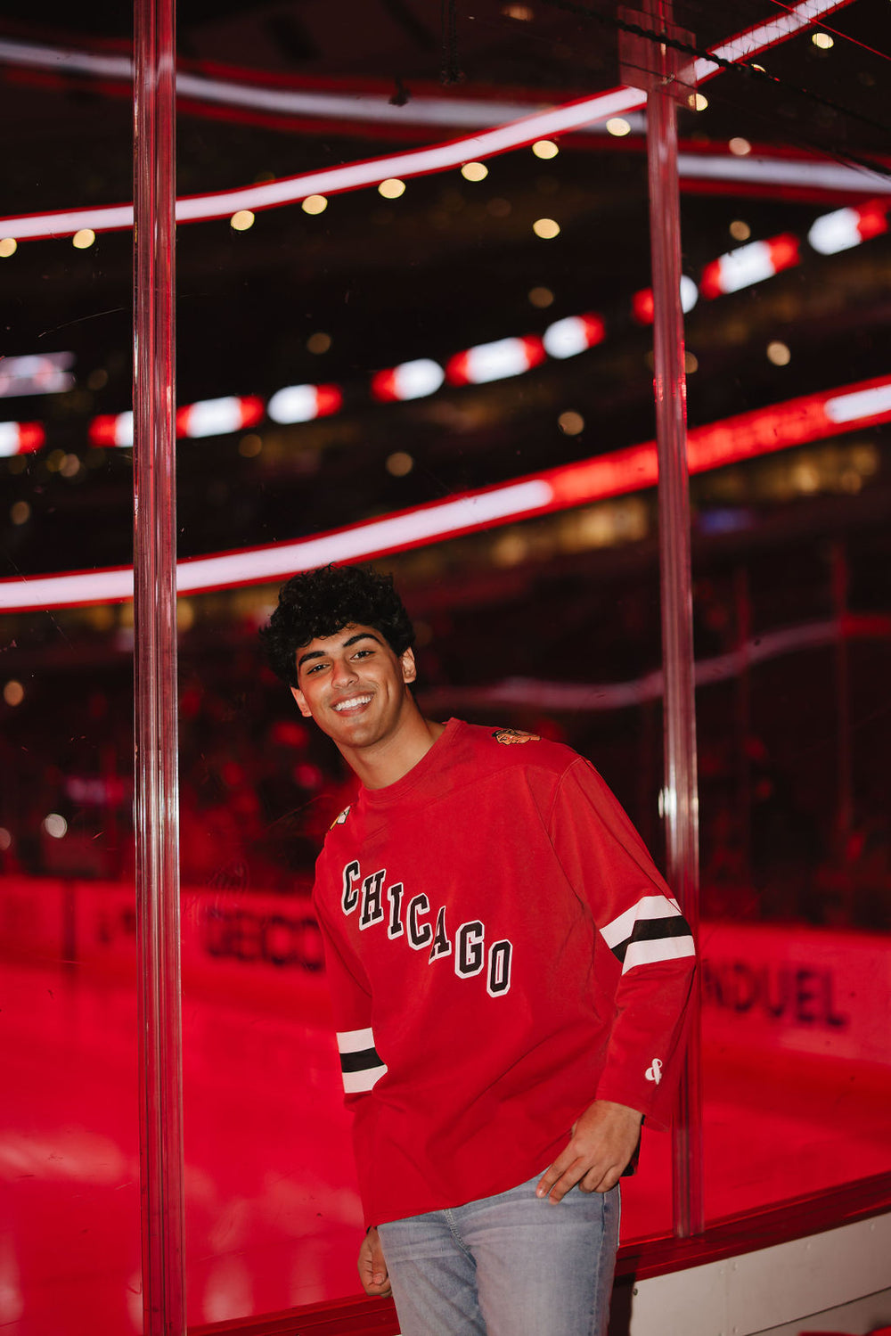 man wearing red Alice & Wonder long sleeve tee with diagonal Chicago wordmark and Chicago Blackhawks secondary and primary logo on shoulders and jersey-inspired stripes on sleeves