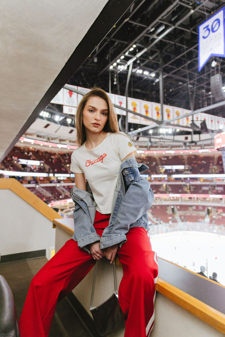 woman wearing cream Alice & Wonder baby tee with red Chicago script graphic across front and Chicago Blackhawks logo on left sleeve