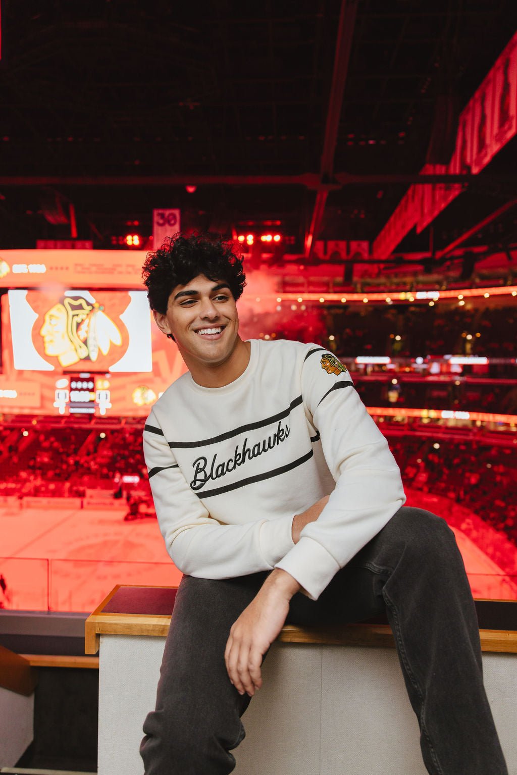 man wearing Alice & Wonder cream crewneck sweater with Blackhawks script graphic on front and Chicago Blackhawks primary logo on left shoulder