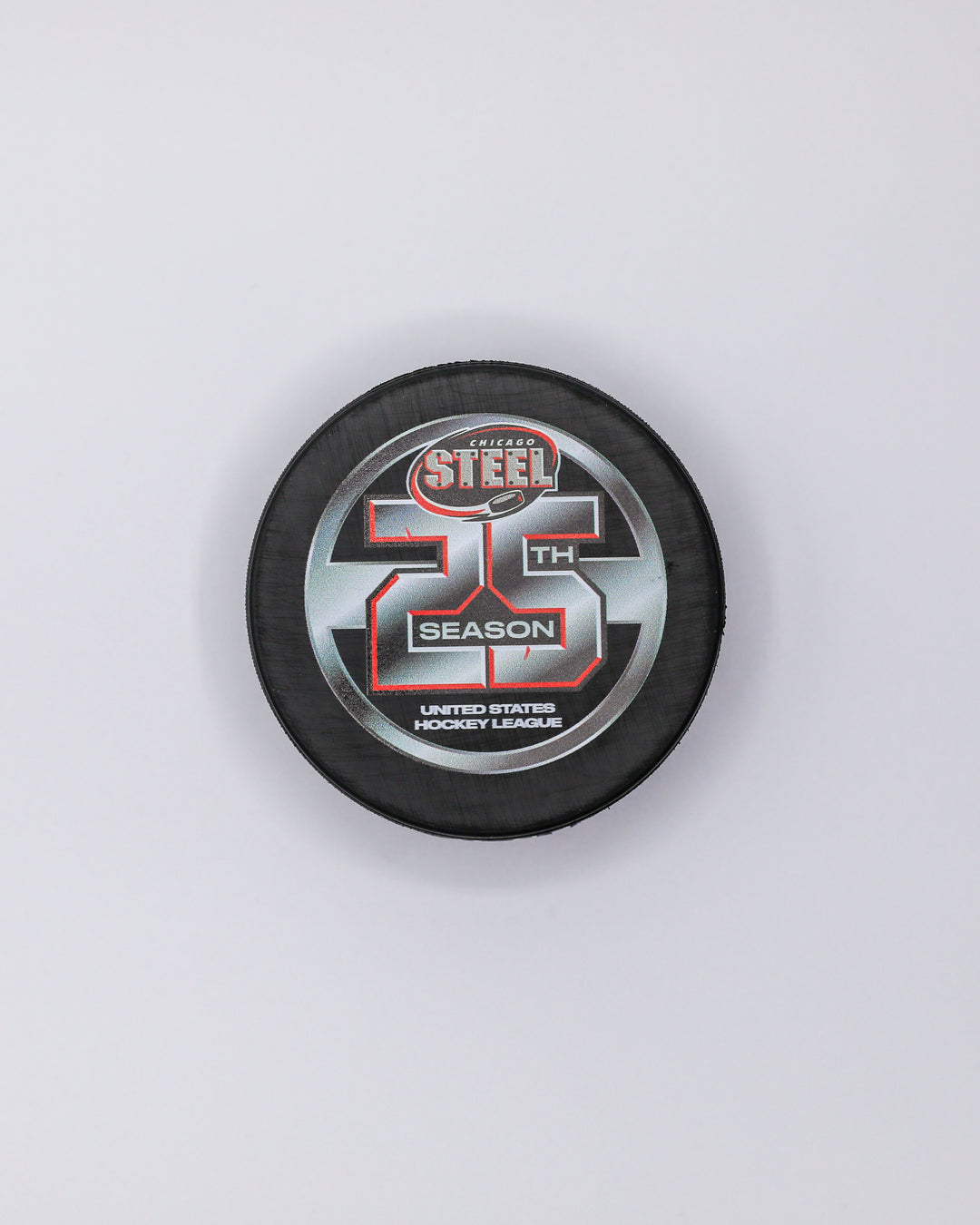 black hockey puck with Chicago Steel logo and 25th season graphic on front - front lay flat