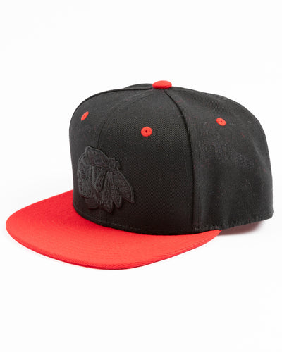 two tone black and red youth snapback cap with Chicago Blackhawks tonal primary logo on front and red wordmark on back - left angle lay flat