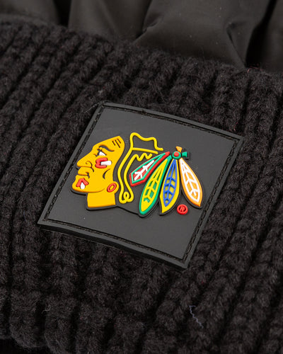 black Zoozatz pom knit hat with puffer jacket fabric on front and knit cuff with Chicago Blackhawks rubberized patch on front - detail lay flat 