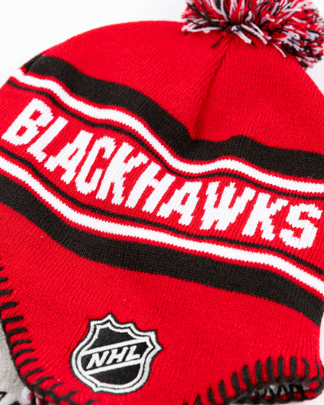 red youth knit hat with tassels and Chicago Blackhawks wordmark on front and Chicago Blackhawks primary logo and NHL logo embroidered on sides - alt detail lay flat