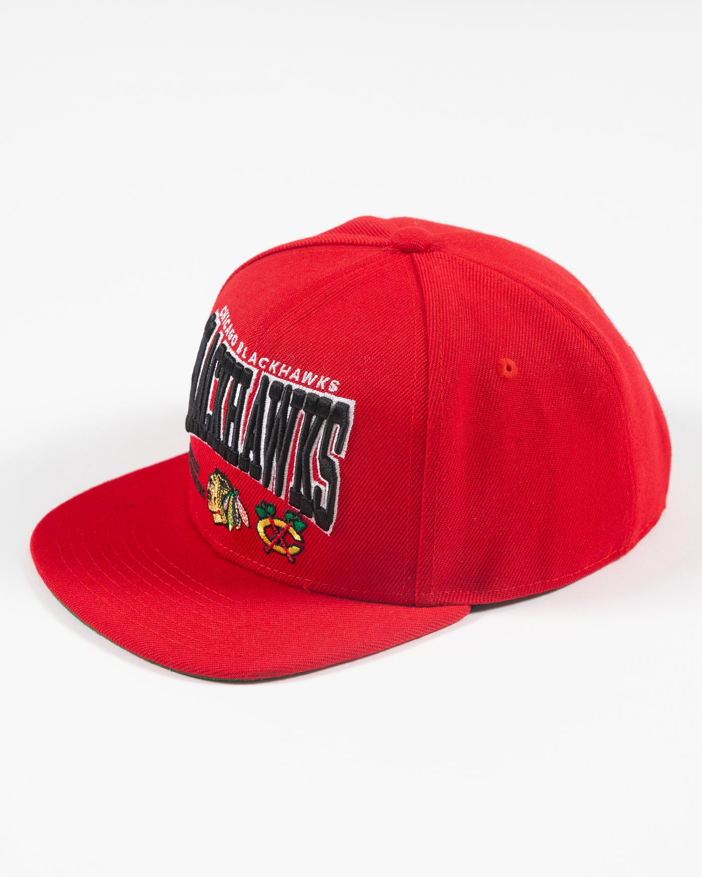 red Mitchell & Ness youth snapback with Chicago Blackhawks wordmark graphic and primary and secondary logos embroidered on front - left angle lay flat