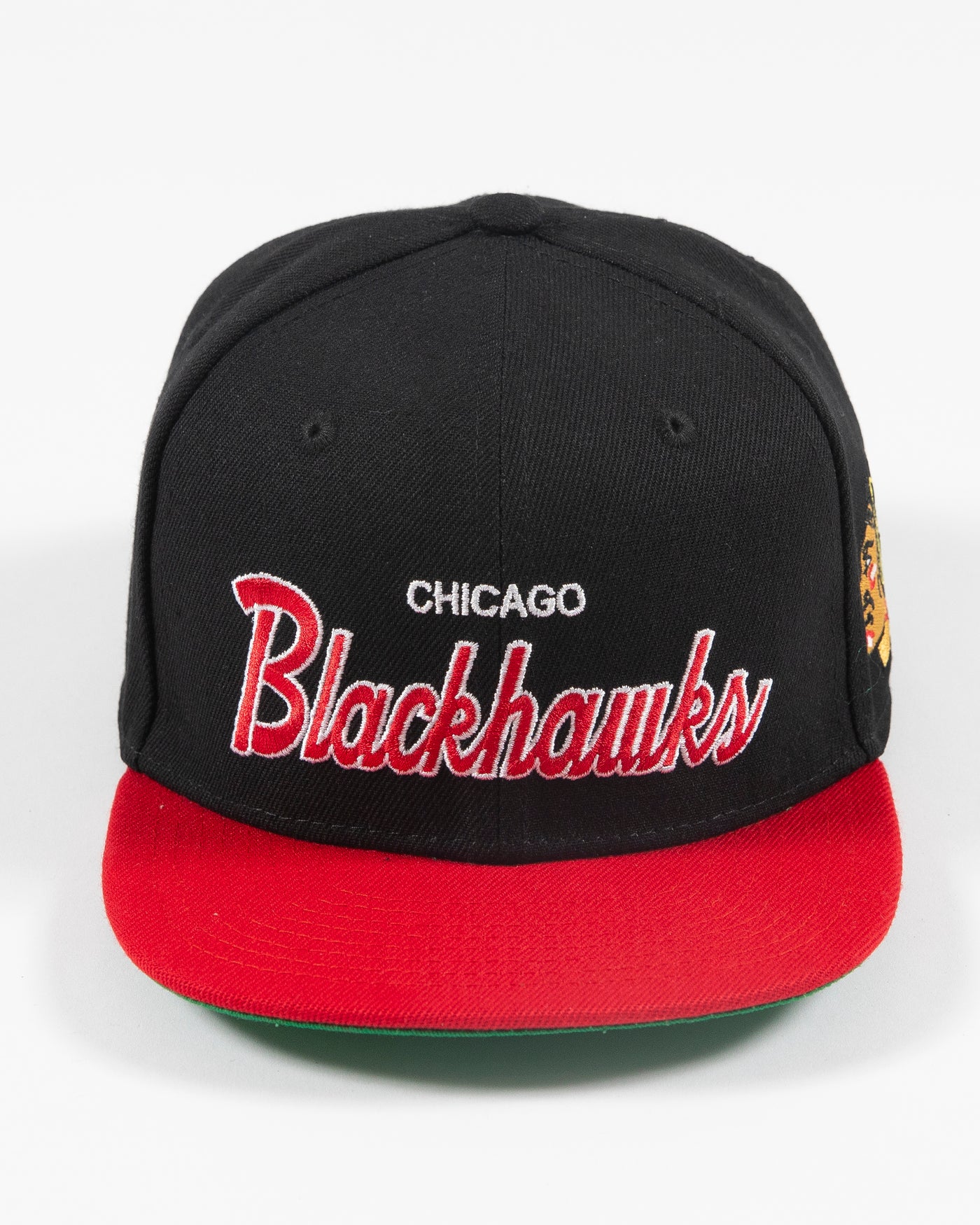 black and red Mitchell & Ness youth snapback cap with Chicago Blackhawks wordmark embroidered on front and primary logo embroidered on left side - front lay flat