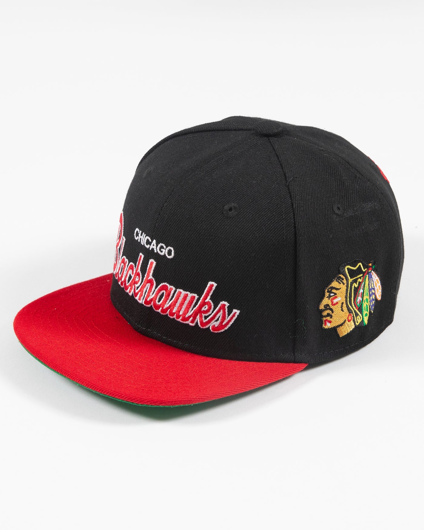 black and red Mitchell & Ness youth snapback cap with Chicago Blackhawks wordmark embroidered on front and primary logo embroidered on left side - left angle lay flat