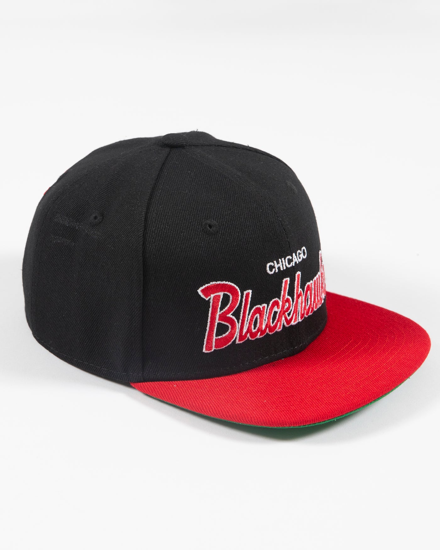 black and red Mitchell & Ness youth snapback cap with Chicago Blackhawks wordmark embroidered on front and primary logo embroidered on left side - right angle lay flat