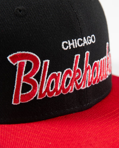 black and red Mitchell & Ness youth snapback cap with Chicago Blackhawks wordmark embroidered on front and primary logo embroidered on left side - detail lay flat