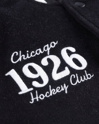 black CCM varsity jacket with Chicago Blackhawks primary logo embroidered on right chest and 1926 wordmark embroidered on left chest - detail wordmark lay flat