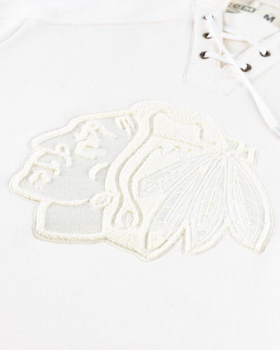 white CCM lace up hoodie with hockey jersey inspired design and Chicago Blackhawks primary logo across front chest - detail lay flat