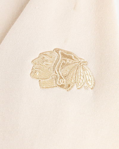 beige cream TravisMathew hoodie with tiny wordmark logo across chest and Chicago Blackhawks primary logo embroidered on left sleeve - logo lay flat