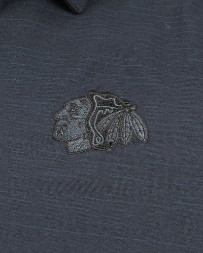 black TravisMathew polo with Chicago Blackhawks tonal primary logo embroidered on left chest - detail lay flat