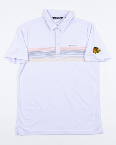 white TravisMathew polo with multicolor stripes and embroidered Chicago Blackhawks primary logo on left shoulder - front lay flat
