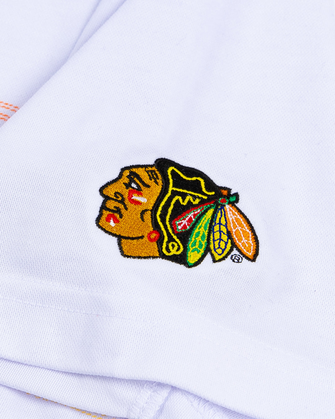 white TravisMathew polo with multicolor stripes and embroidered Chicago Blackhawks primary logo on left shoulder - detail lay flat