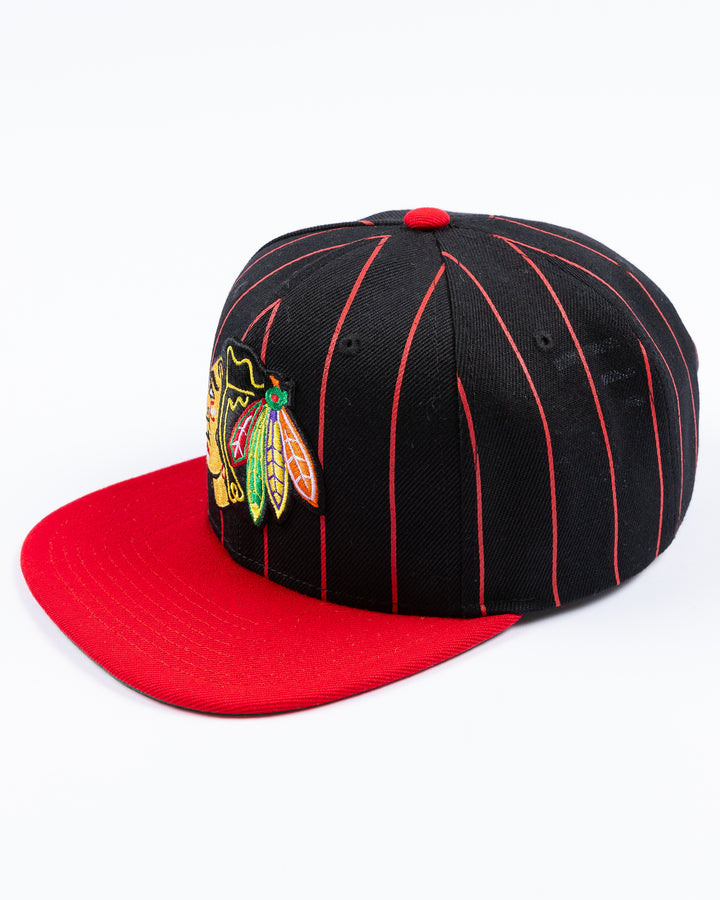 black and red Mitchell & Ness snapback cap with embroidered Chicago Blackhawks primary logo embroidered on front - left angle lay flat