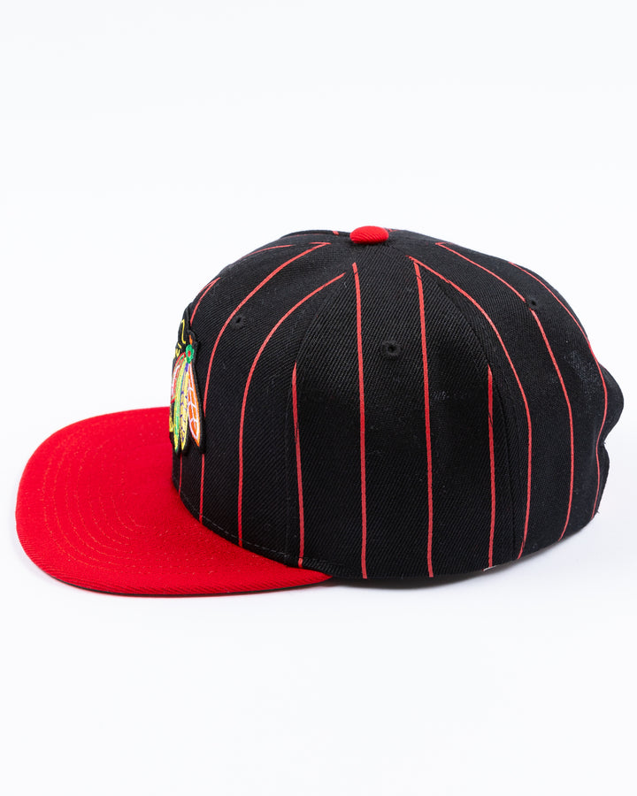 black and red Mitchell & Ness snapback cap with embroidered Chicago Blackhawks primary logo embroidered on front - left side lay flat