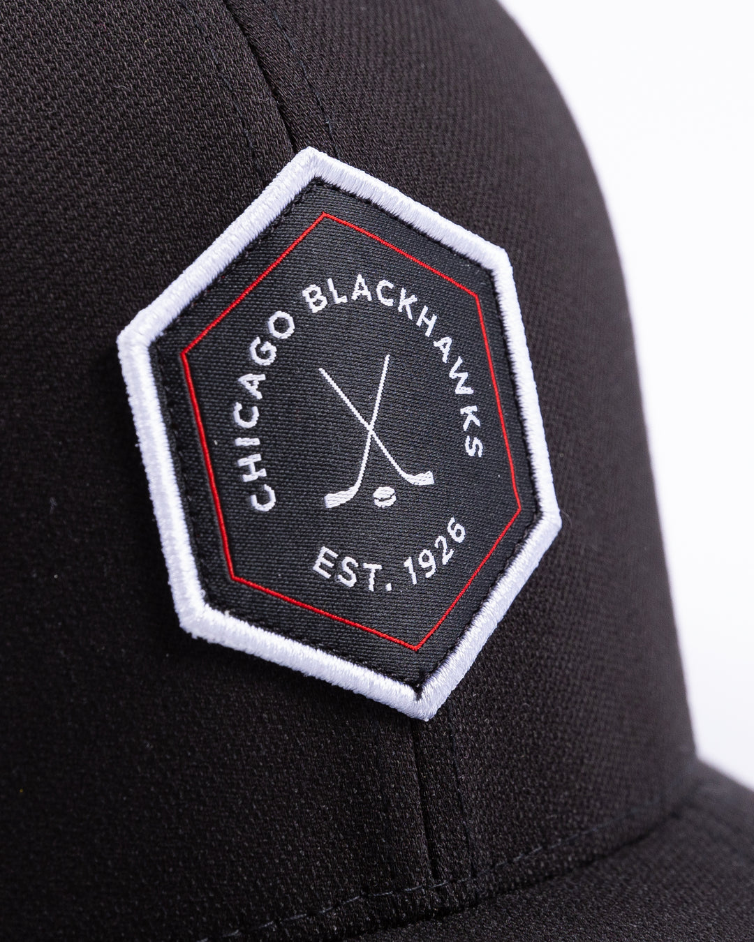 black TravisMathew adjustable cap with hexagon patch on front and Chicago Blackhawks wordmark and crossed hockey sticks graphic - front detail lay flat