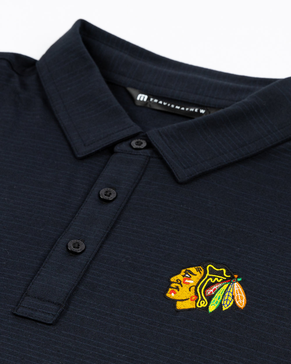 black TravisMathew polo with Chicago Blackhawks primary logo embroidered on left chest - detail lay flat