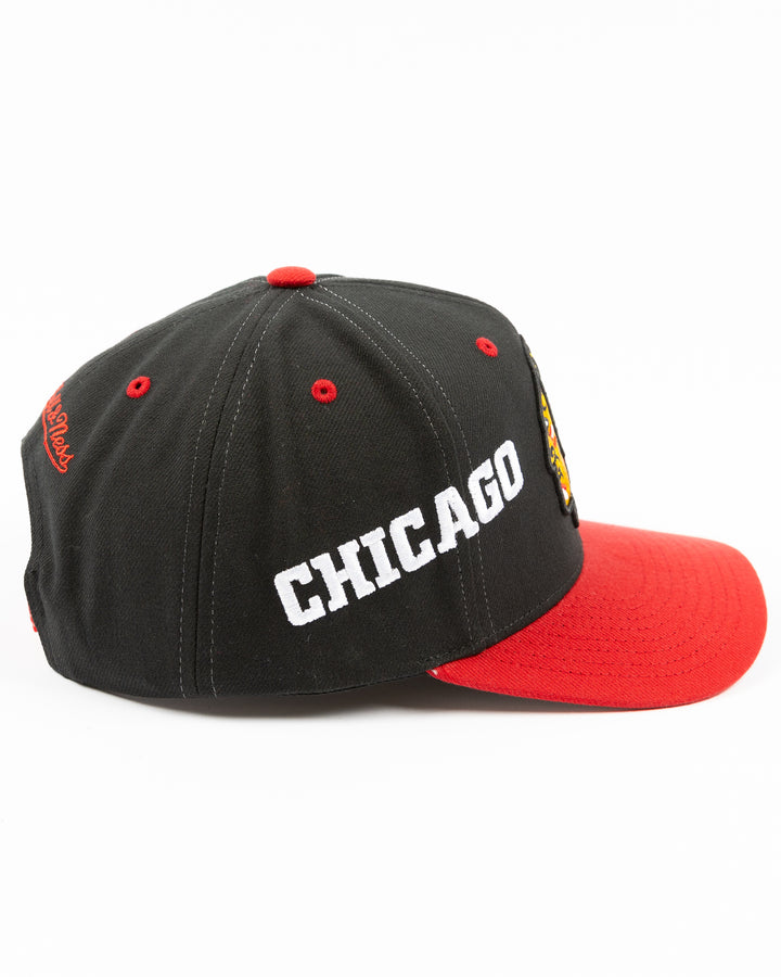 black and red Mitchell & Ness snapback with Chicago Blackhawks primary logo on front, secondary logo on left side and wordmark Chicago on right - right side lay flat