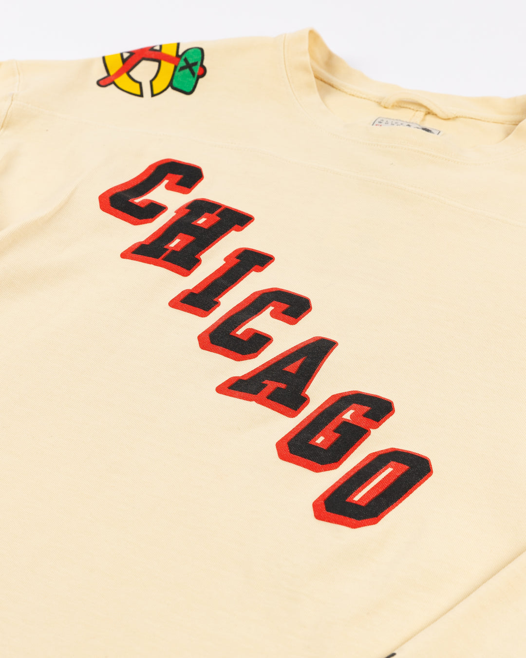 cream Alice & Wonder long sleeve tee with diagonal Chicago wordmark graphic and Chicago Blackhawks secondary and primary logo on shoulders with jersey stripes on sleeves - front detail lay flat