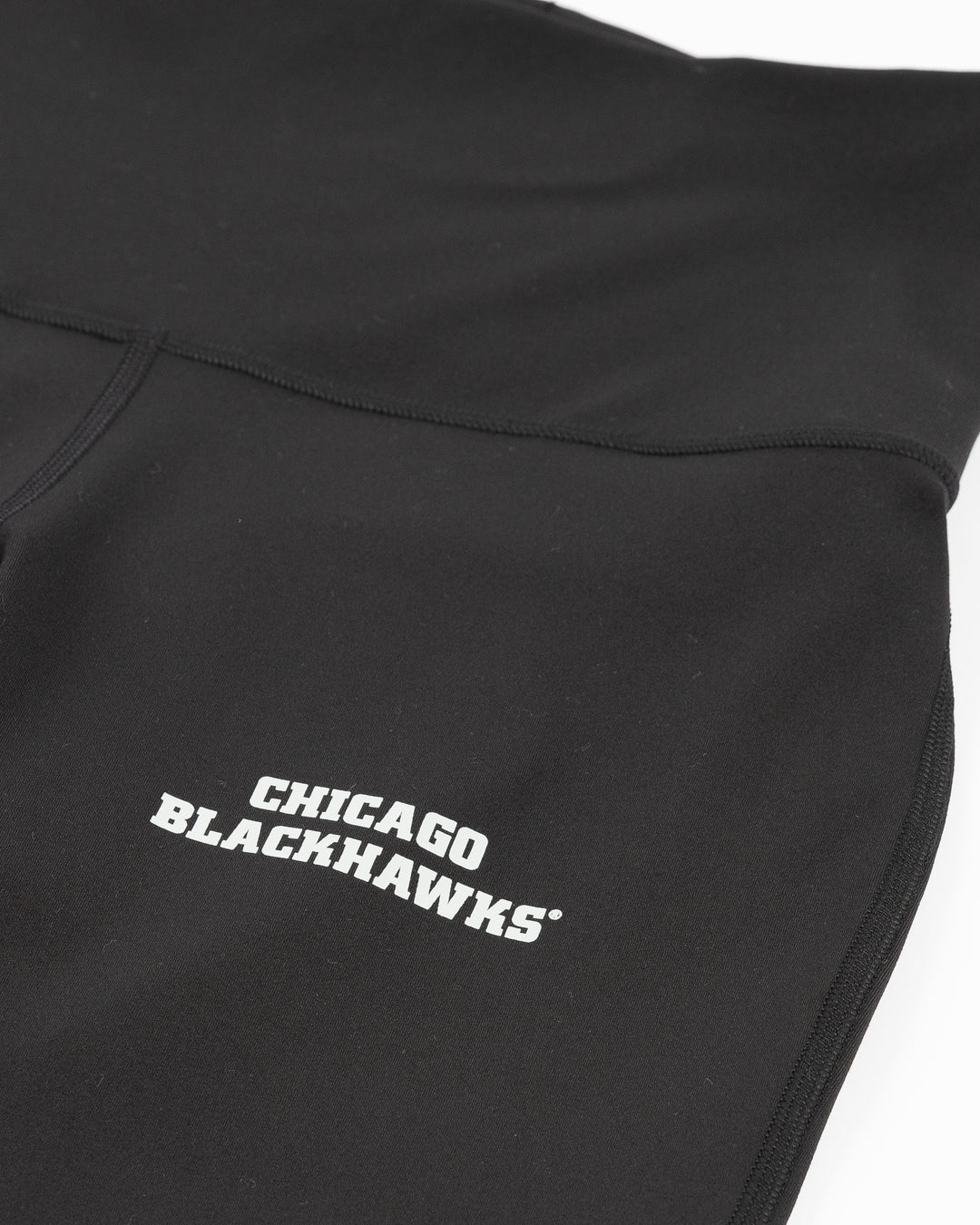 black lululemon legging pants with flare at hem and Chicago Blackhawks wordmark on left thigh - front detail lay flat