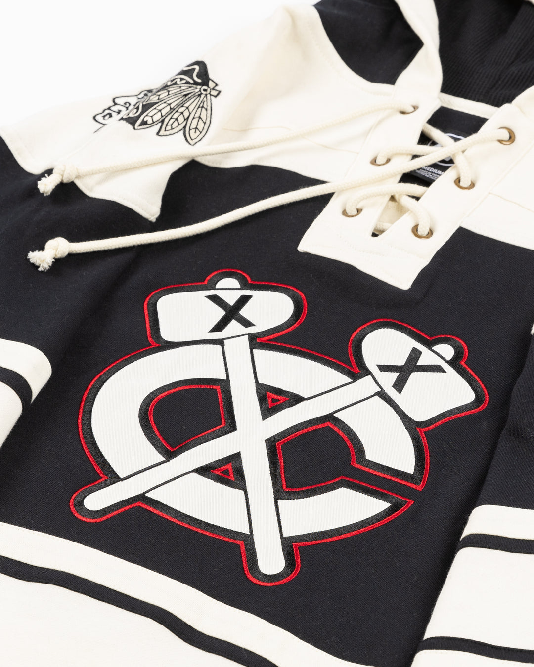 black and cream '47 brand lacer hoodie with Chicago Blackhawks secondary logo on front and primary logo on shoulders - front detail lay flat