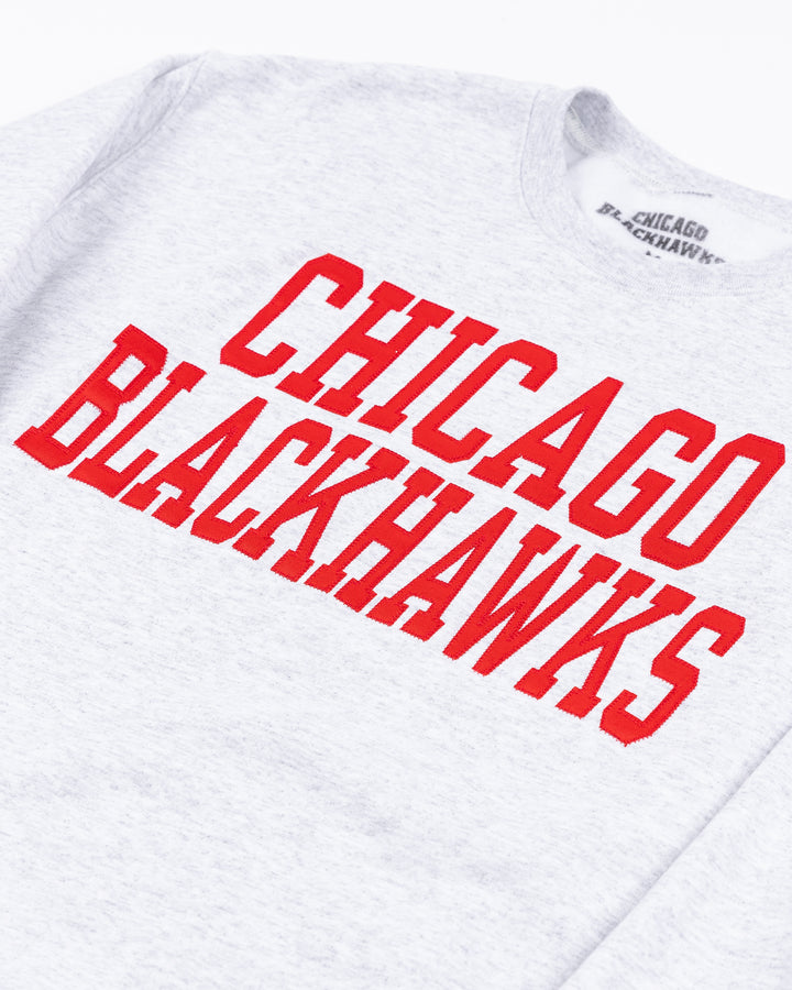 light grey crewneck sweatshirt with Chicago Blackhawks wordmark in red across front and Chicago Blackhawks secondary logo on left cuff - front detail lay flat