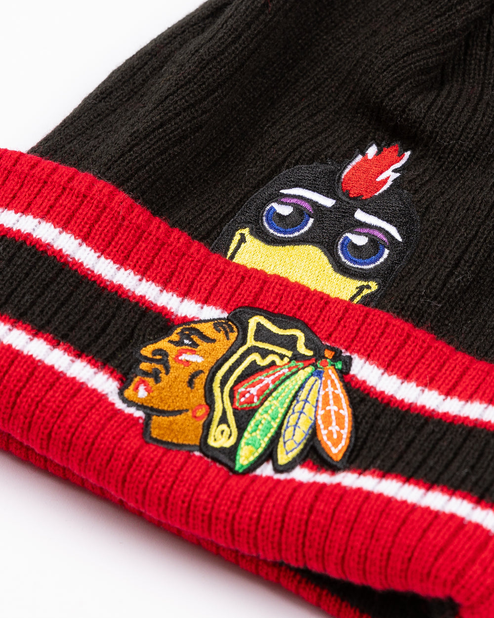 black and red infant knit beanie with red pom with Chicago Blackhawks mascot Tommy Hawk on front and primary logo on cuff  - front detail lay flat