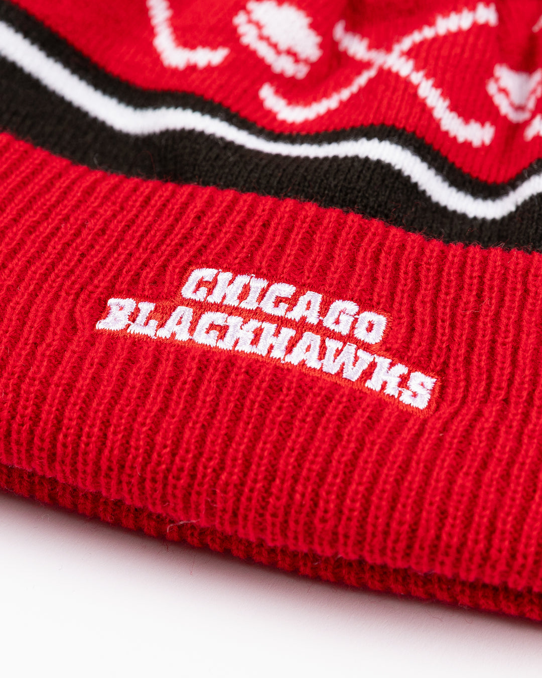 red white and black infant sized knit beanie with red and white pom and hockey stick and puck graphic with Chicago Blackhawk primary logo embroidered on front cuff - back detail lay flat