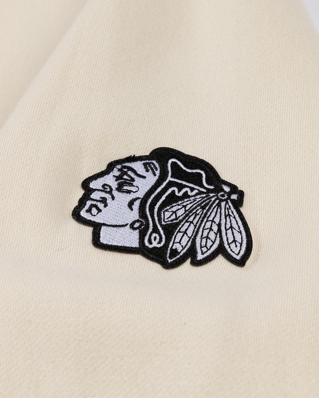 cream CCM crewneck sweater with tonal Chicago Blackhawks wordmark across front and black and white primary logo embroidered on left shoulder - shoulder detail lay flat