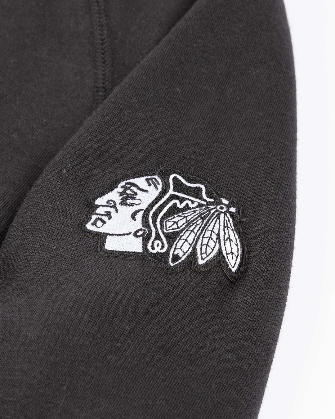 black CCM crewneck sweater with tonal Chicago Blackhawks wordmark across front and black and white primary logo embroidered on left shoulder - shoulder detail lay flat