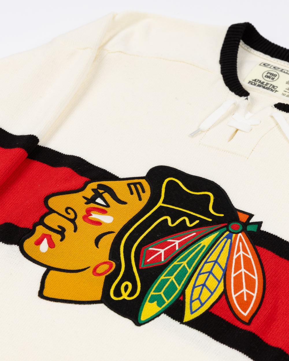 white CCM sweater with red and black stripe on center with Chicago Blackhawks primary logo across front with lace neck details - front detail lay flat