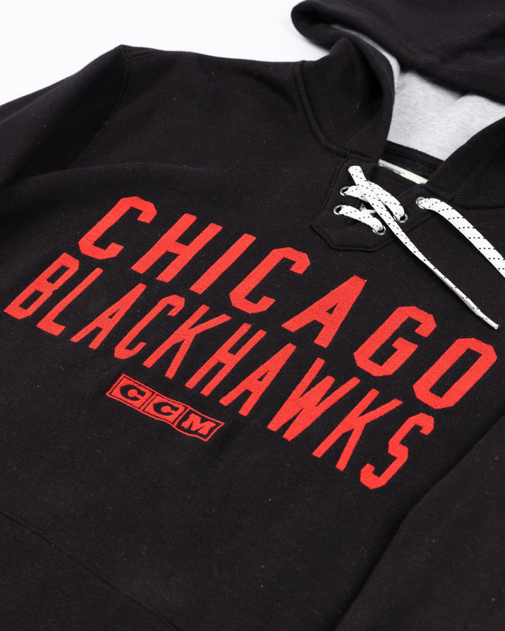 black CCM lacer hoodie with red Chicago Blackhawks wordmark across front and vintage Chicago Blackhawks logo on left shoulder - front detail lay flat