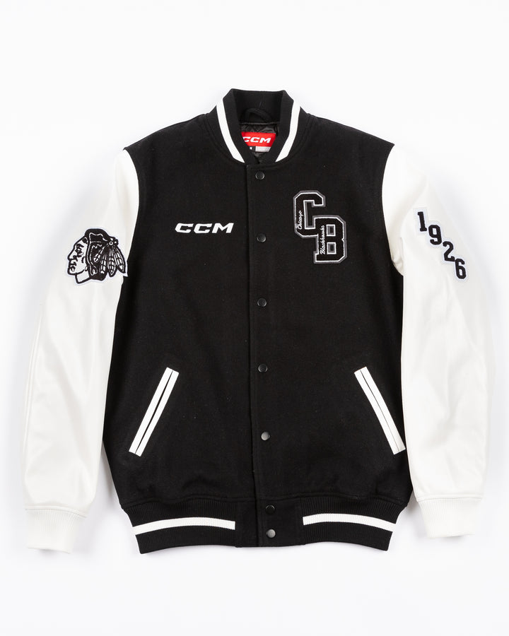 black and white CCM varsity jacket with Chicago Blackhawks primary logo on right shoulder and CCM logo embroidered on right chest and CB patch on left chest and 1926 embroidered on left shoulder - front lay flat