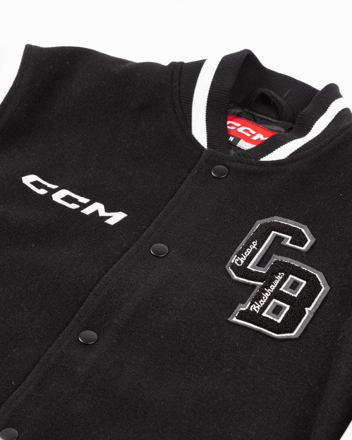 black and white CCM varsity jacket with Chicago Blackhawks primary logo on right shoulder and CCM logo embroidered on right chest and CB patch on left chest and 1926 embroidered on left shoulder - front detail lay flat