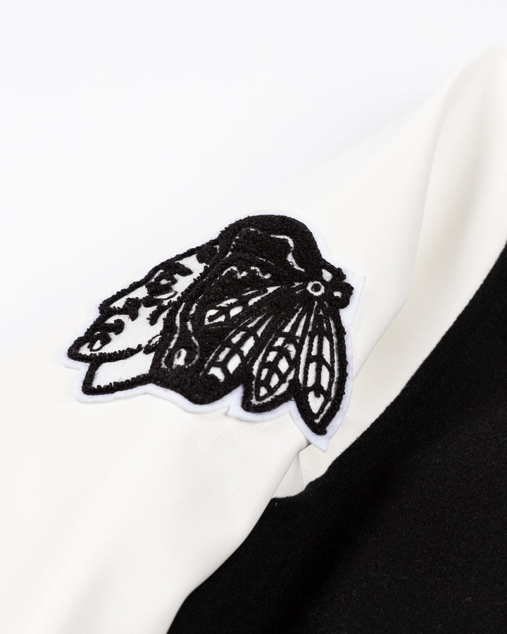 black and white CCM varsity jacket with Chicago Blackhawks primary logo on right shoulder and CCM logo embroidered on right chest and CB patch on left chest and 1926 embroidered on left shoulder - primary logo detail lay flat