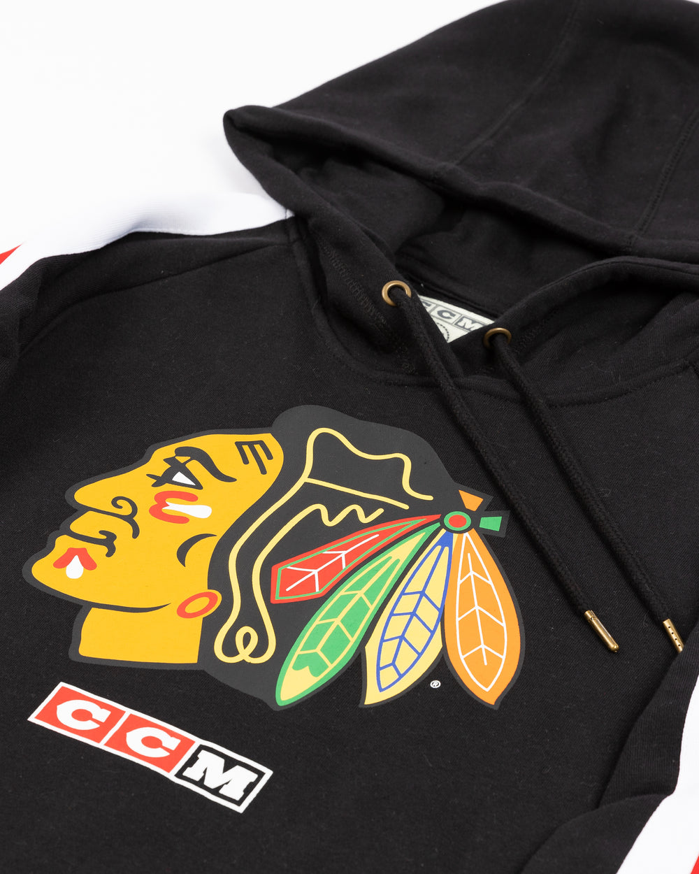 black CCM hoodie with red and white stripes on shoulders and Chicago Blackhawks primary logo on front - front detail lay flat