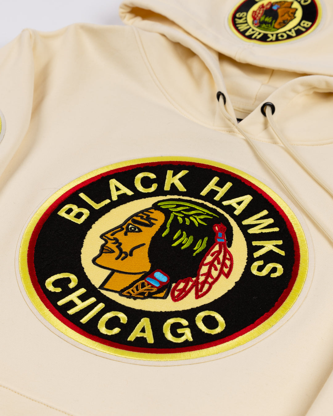 cream Pro Standard hoodie with black striping on hem and cuffs and vintage Chicago Blackhawks logo patches on front, hood and shoulders - front detail lay flat