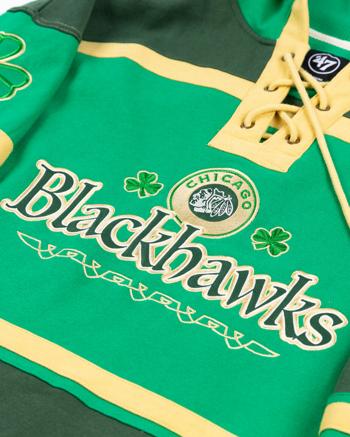 green and gold '47 brand hockey jersey inspired lacer hoodie with Irish inspired Blackhawks design on front and shamrocks on sleeves - front detail lay flat