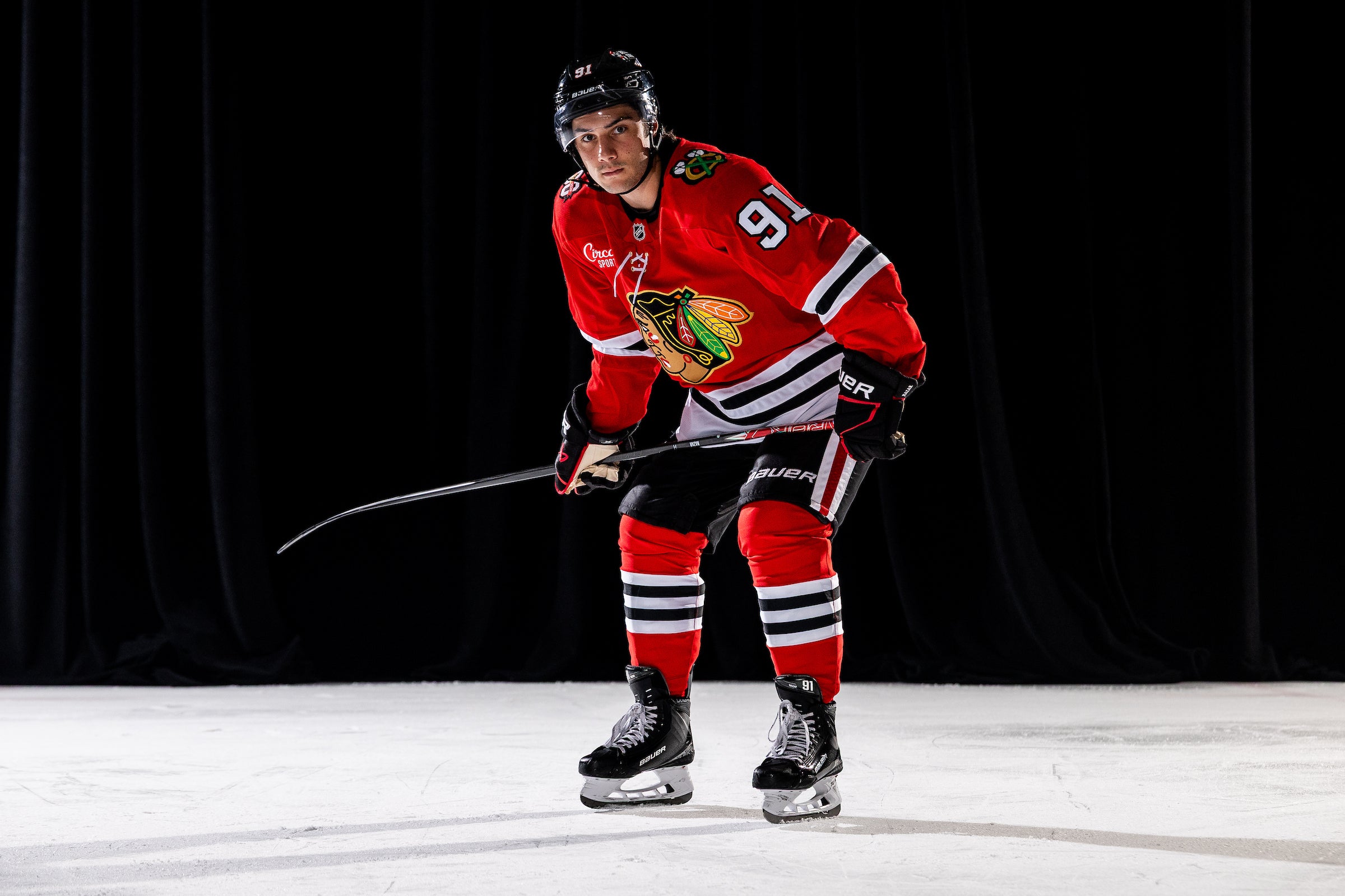 Hockey player in a red uniform with a black helmet on an ice rink.