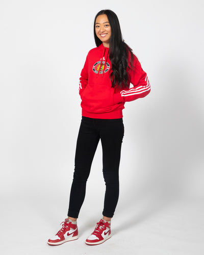 Red adidas hoodie with primary logo on center chest and three white stripes going down both arms - side view on model
