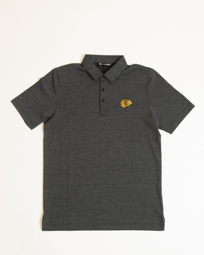 dark grey TravisMathew polo with button closure and embroidered Chicago Blackhawks primary logo on left chest - front lay flat