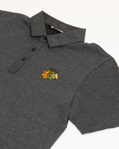 dark grey TravisMathew polo with button closure and embroidered Chicago Blackhawks primary logo on left chest - detail lay flat